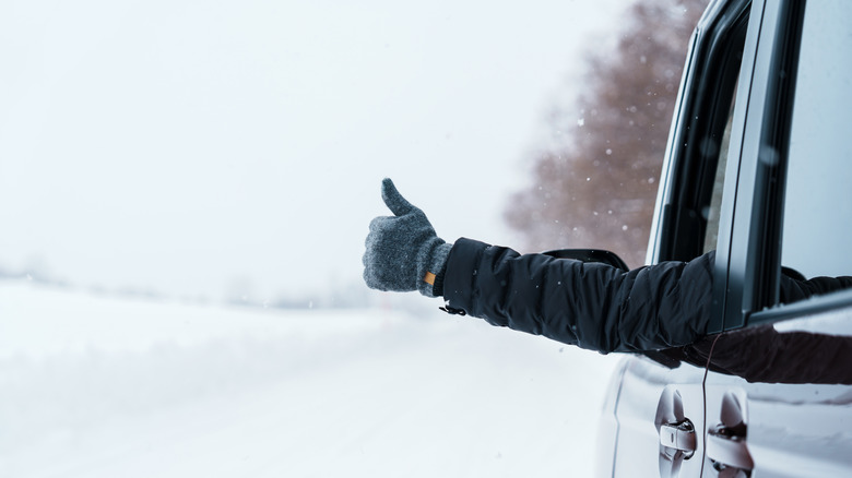 A traveler in a car sticking a thumbs up out of a window with snowy weather