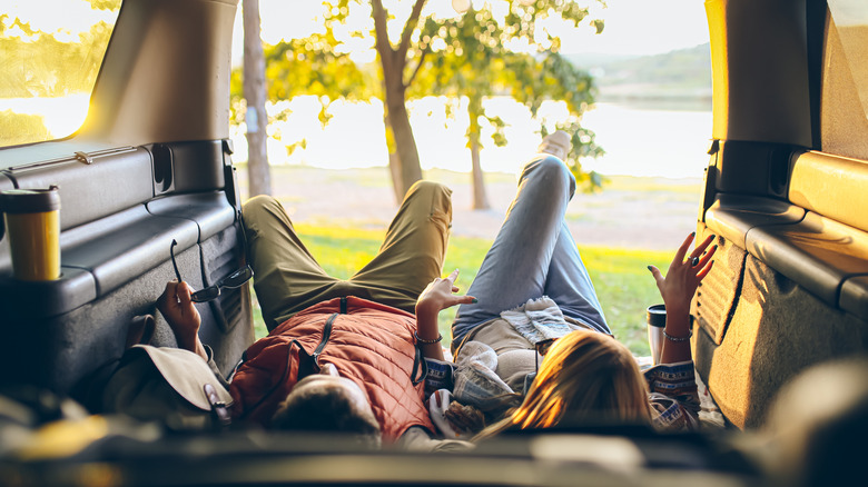 Two people lying down in the cargo area of a car while camping.