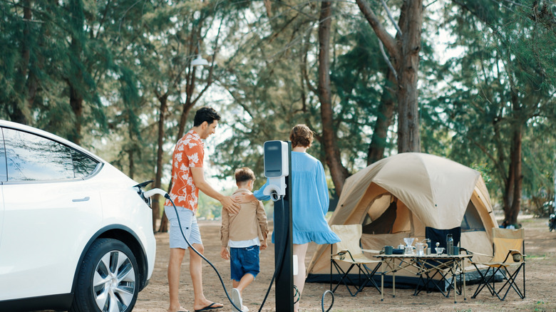 A family charging an electric vehicle by a campsite.