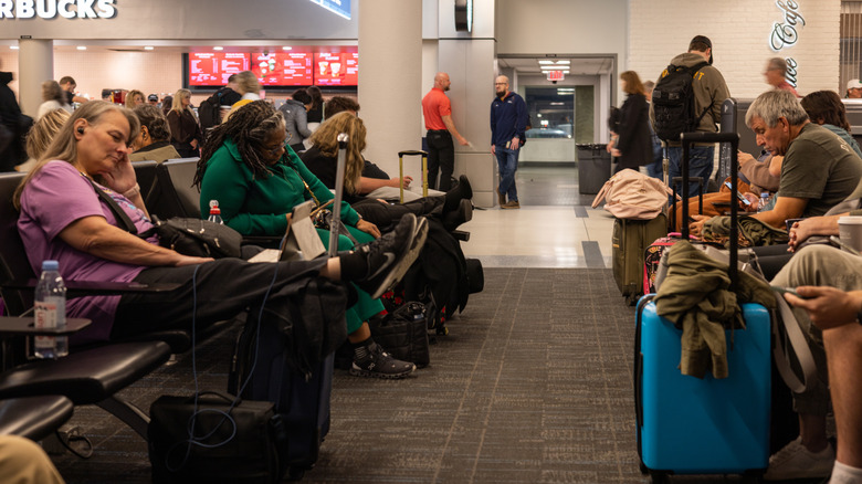 a crowded airport terminal with passengers sitting waiting for their connecting flights