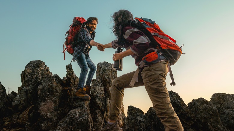 Two hikers help each other over jagged rocks