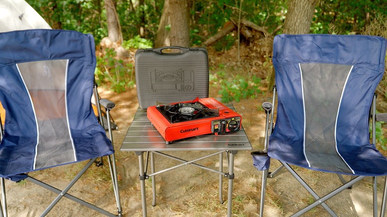 Cuisinart portable camping stove on a table between two chairs.