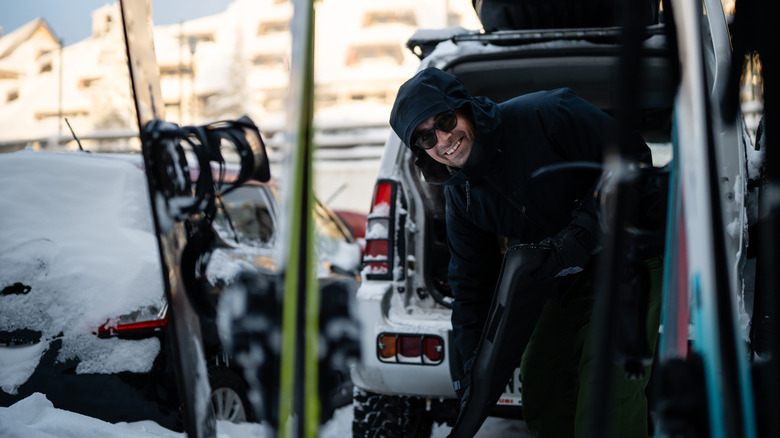 Happy man smiling while packing skis and gear into a car trunk on a snowy winter day