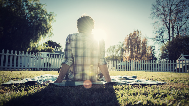 The back of a person sitting on a blanket on their lawn.