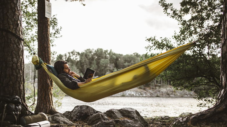 Person sits in their hammock in the woods reading
