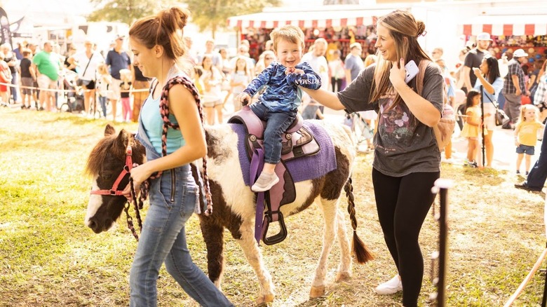 Smiling hild on a horse with two women assisting