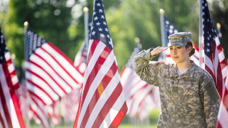 A young female soldier saluting near American flags.