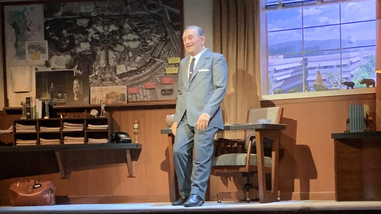 Animatronic Walt Disney leaning on his desk onstage.