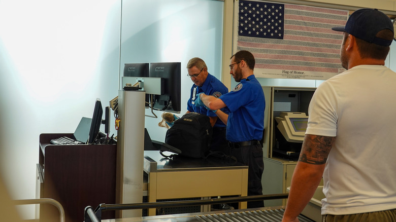 Two TSA security employees checking a backpack at a security checkpoint