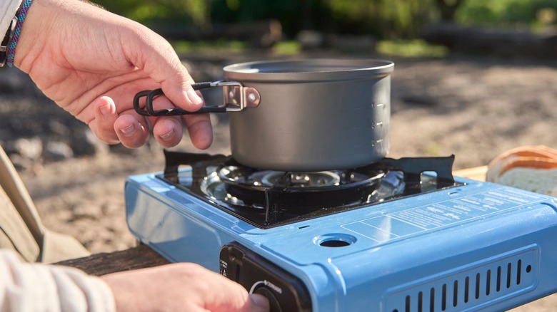 Person lighting camping stove with pot on it