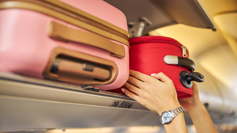Arms shoving a small piece of luggage to the top shelf of an aircraft