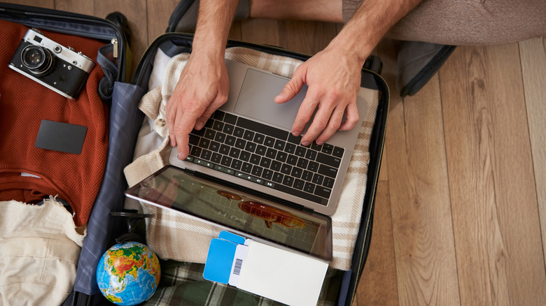 An open, packed suitcase with a person working on a laptop set atop the suitcase