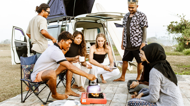 A diverse group of young travelers cooks in front of a campervan