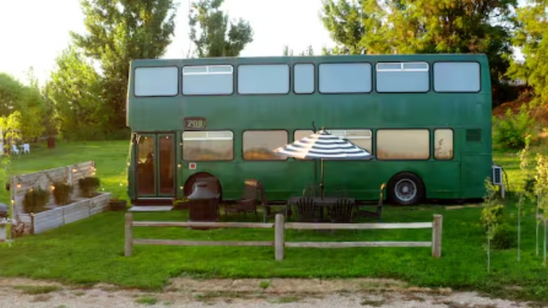 A green double decker bus coverted into an airbnb sitting in the middle of a tree lined garden