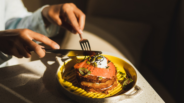 Woman's hands cutting pancakes and fish with a knife and fork
