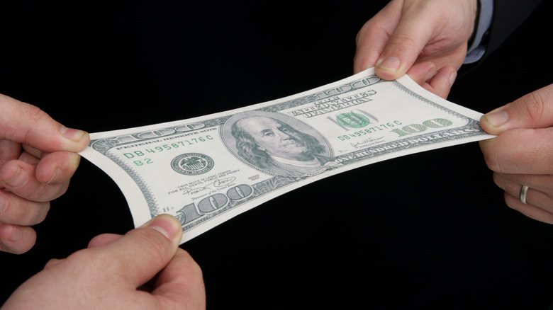 Two pairs of human hands stretching a hundred dollar bill