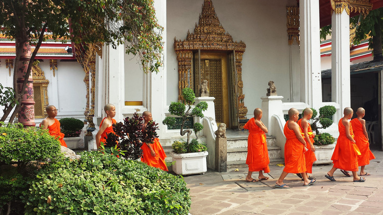 A group of young monks wearing orange robes walking around the temple grounds in Thailand.