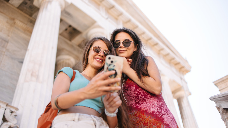 Two female friends in front of a National Library of Greece in Athens looking at the phone