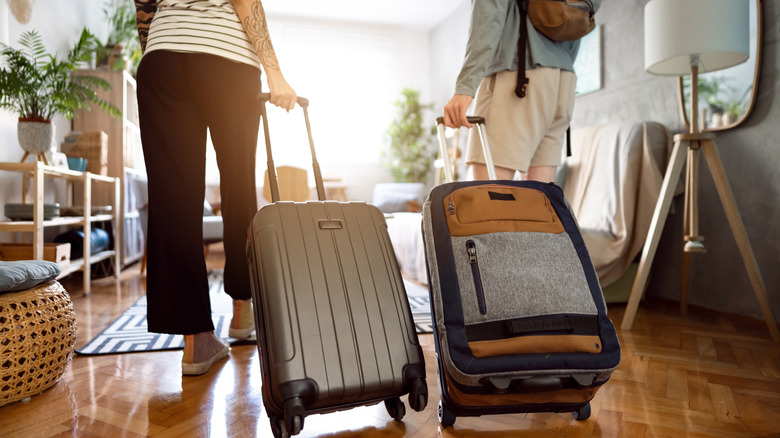 Two people carrying suitcases in a sunny room