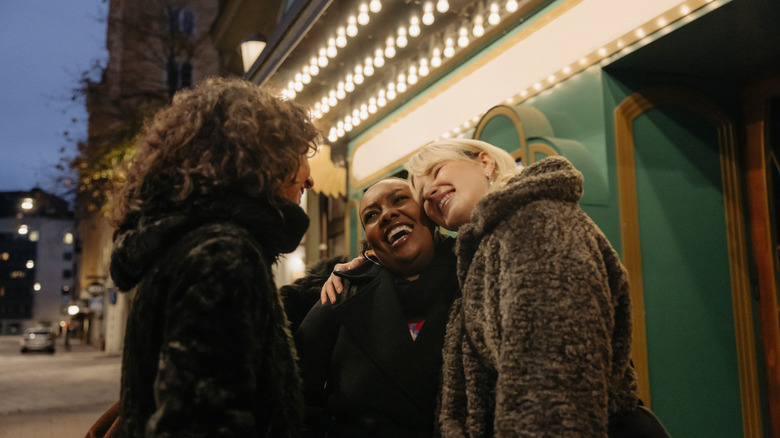 Three friends smiling outside of a brightly lit cinema