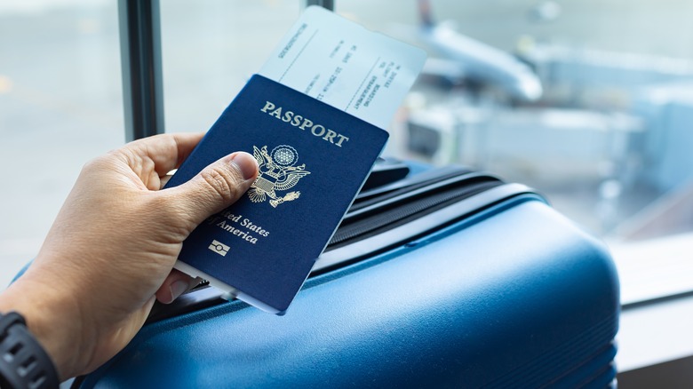 hand holding U.S. passport at airport with suitcase