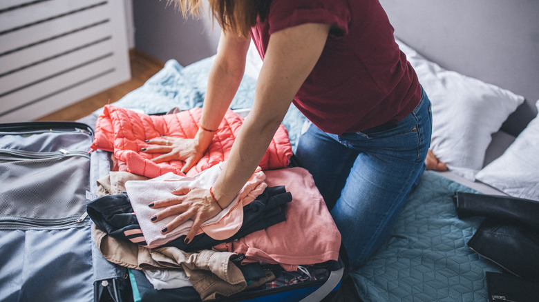 woman pressing clothes into suitcase