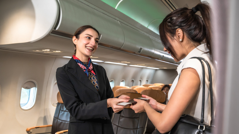 A flight attendant checks passport and boarding pass from a passenger on board.