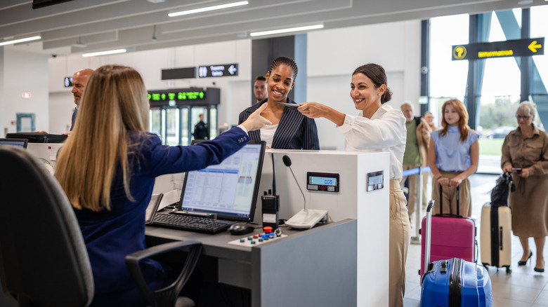 Two women hand their travel documents to a check-in staff member at an airport counter.