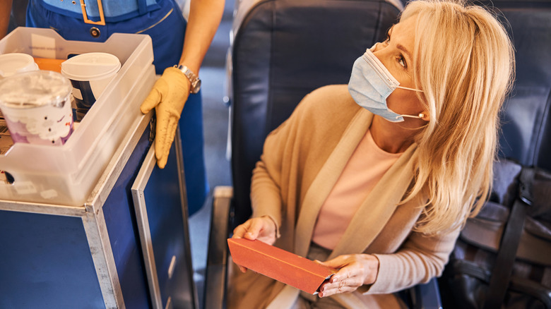 A woman throwing away a biscuit package to a trash trolley of a flight attendant