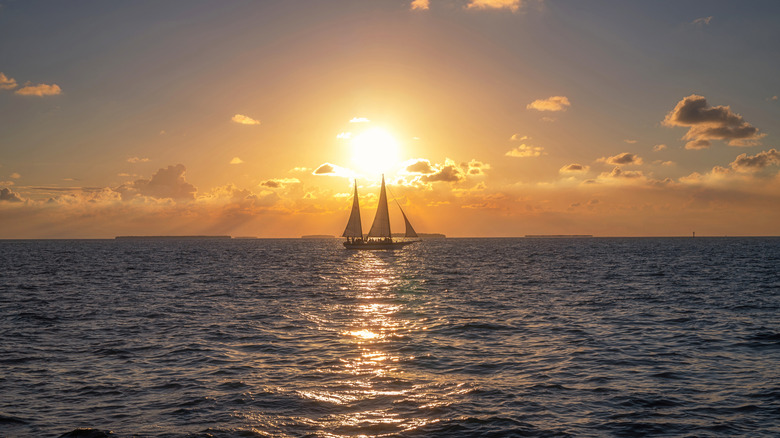 a sailing boat on the horizon against the sunset