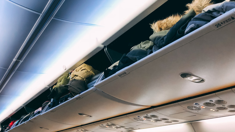 Overhead bins stuffed with coats.