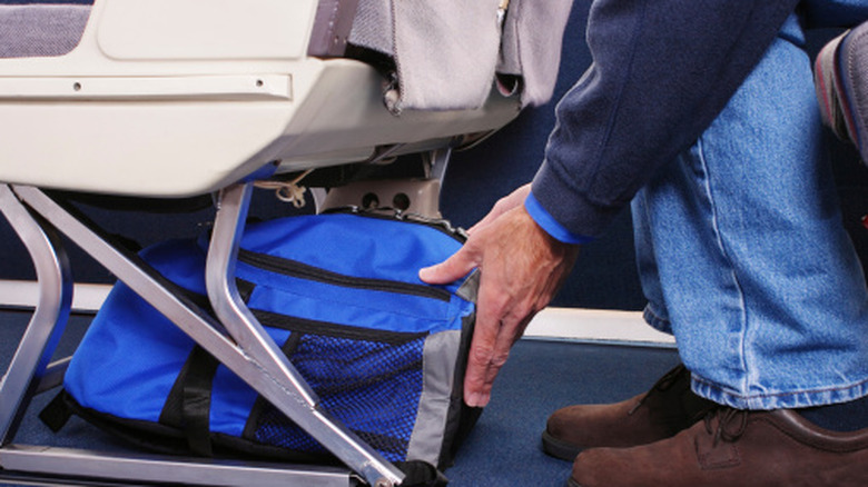 Hands stowing a bag under an airplane seat.