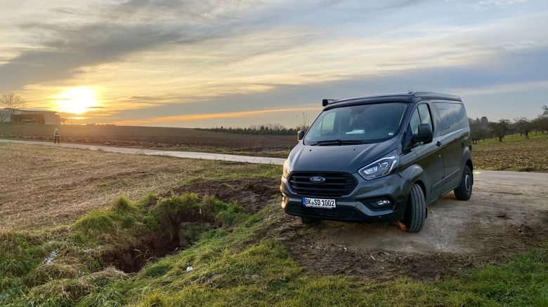 A Ford camper van parked on the side of the road at sunset.
