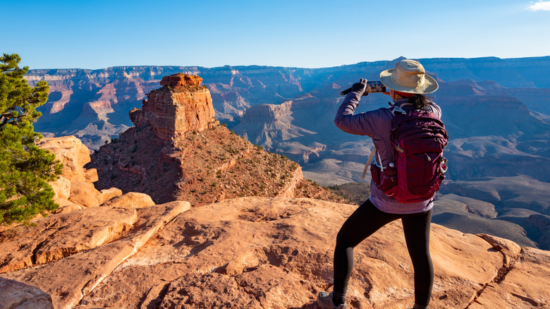 a woman standing on the Grand Canyon's south rim takes a photo with her phone
