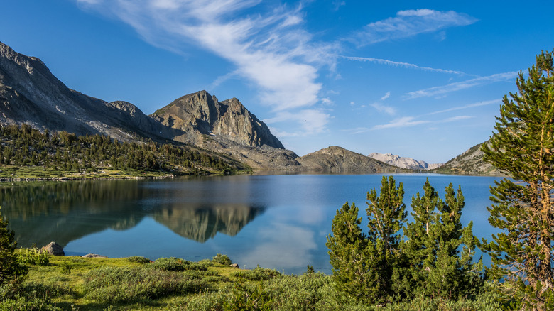 A clear lake (Duck Lake) with mountains in the background and trees and grass around it