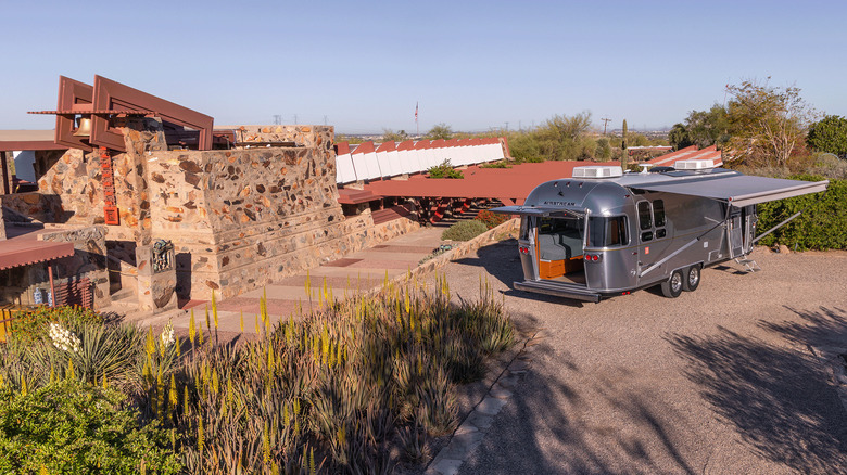 An Airstream next to a stone structure.