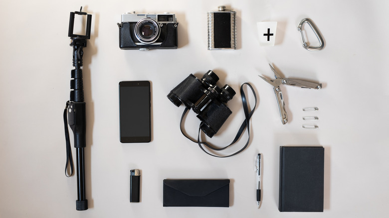 A flat lay of travel items includes camera, binoculars, and a diary