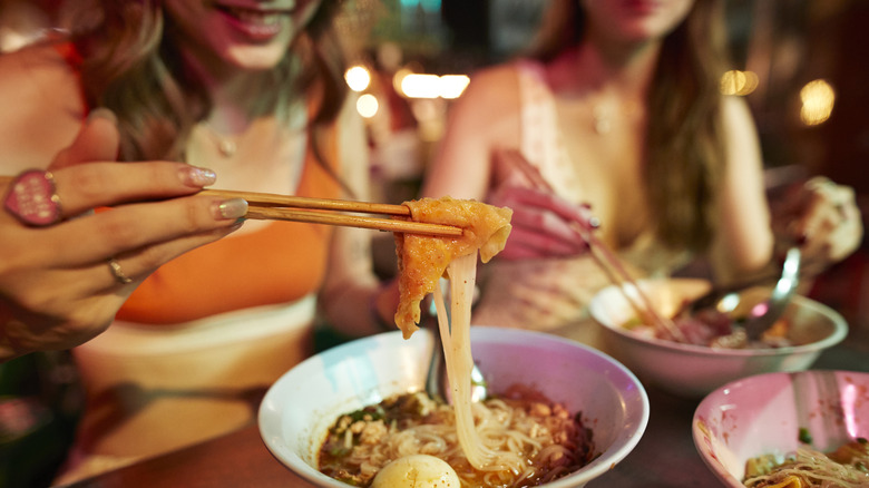 A woman eats noodles with chopsticks