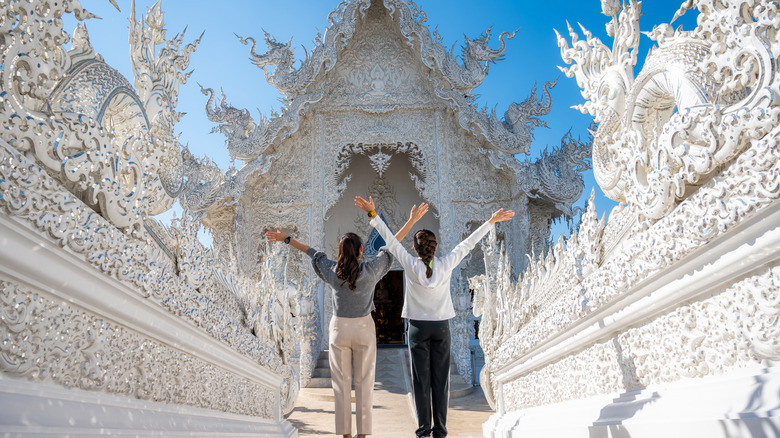 Two young women pose in front of the ornate White Temple