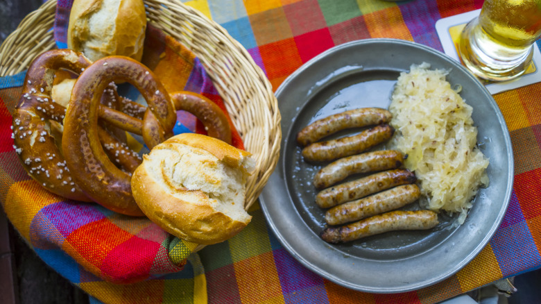 A basket of pretzels and bread rolls next to a plate of sausage and sauerkraut