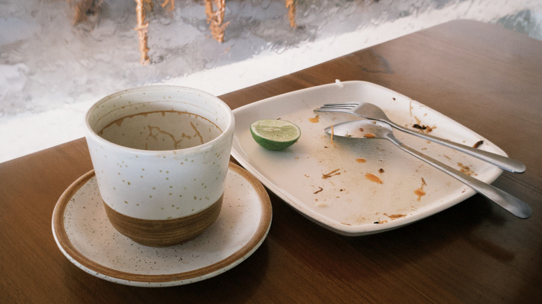 Plates, cup, and cutlery are stacked together after eating at a restaurant