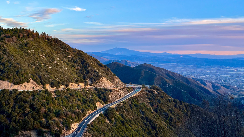 A road winding through the San Bernardino Mountains and overlooking a city at dusk in the distance