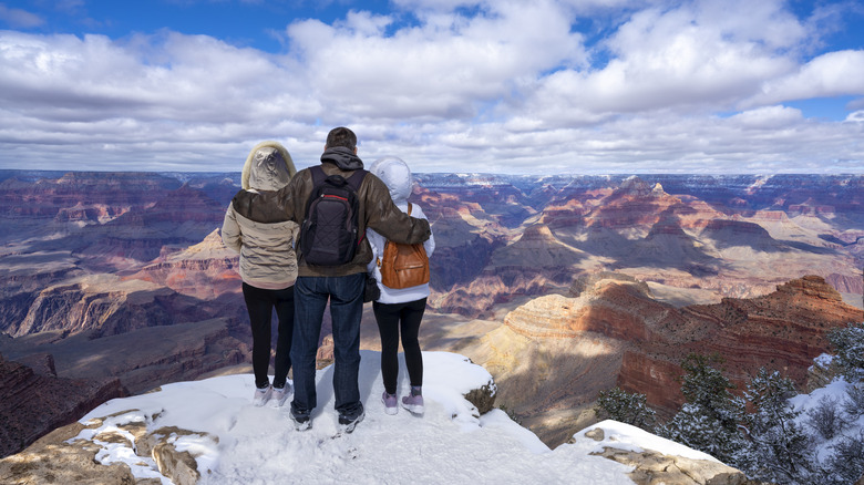 Three people admire the Grand Canyon from a snowy ledge