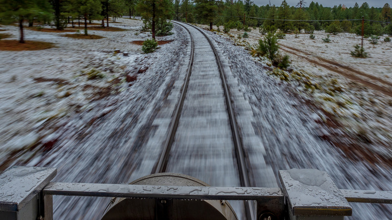 Snowy train tracks whisk past the front of a train engine