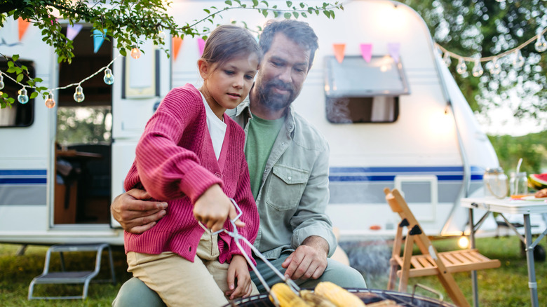 dad and daughter grilling food by campervan