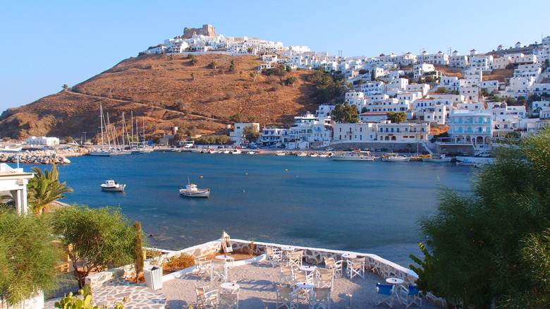 A bay in a Greek island with tables in the foreground and white house in the background