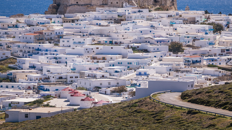 A Greek island village of white houses on a hill with a castle on top