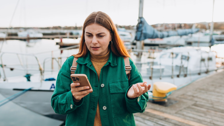 A woman on a dock looks irritably at her cell phone.