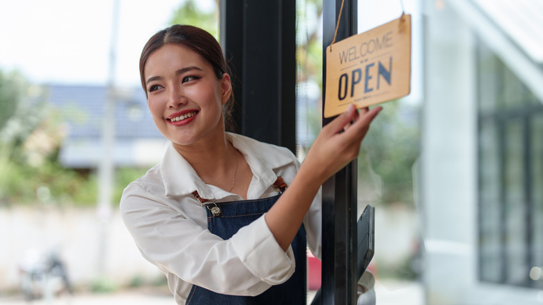 beautiful girl holding open sign in front of a coffee shop