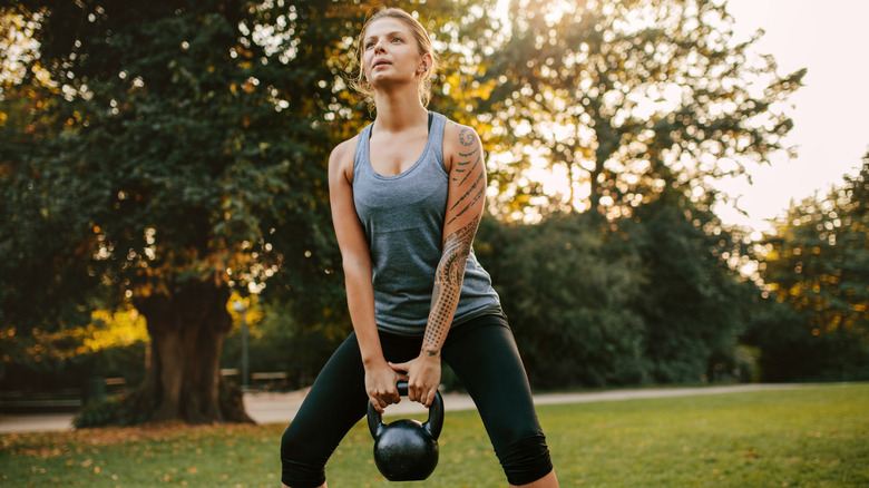 Young woman exercising with kettlebell weights in the park